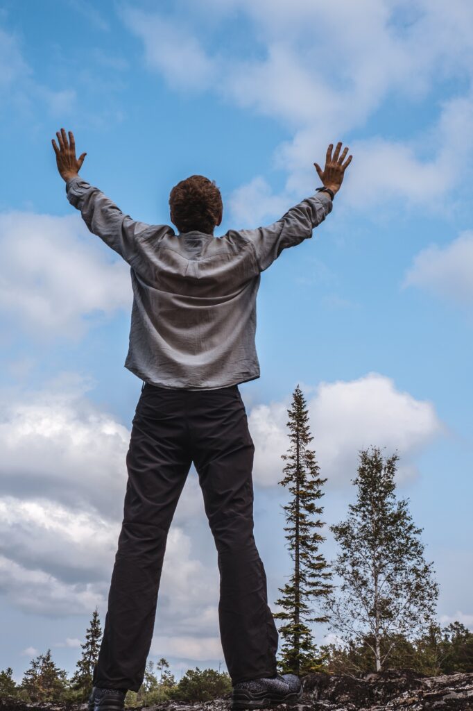 A man on top of mountain against the background of the sky with raised hands, celebrating a victory.
