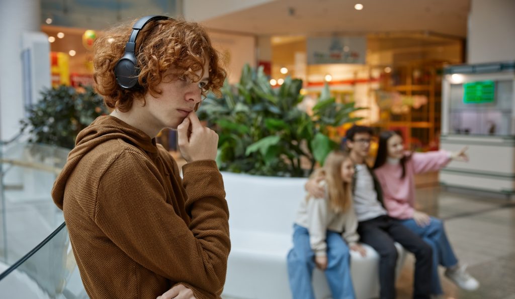 Portrait of sad serious teenager guy wearing headphones alone at shopping mall